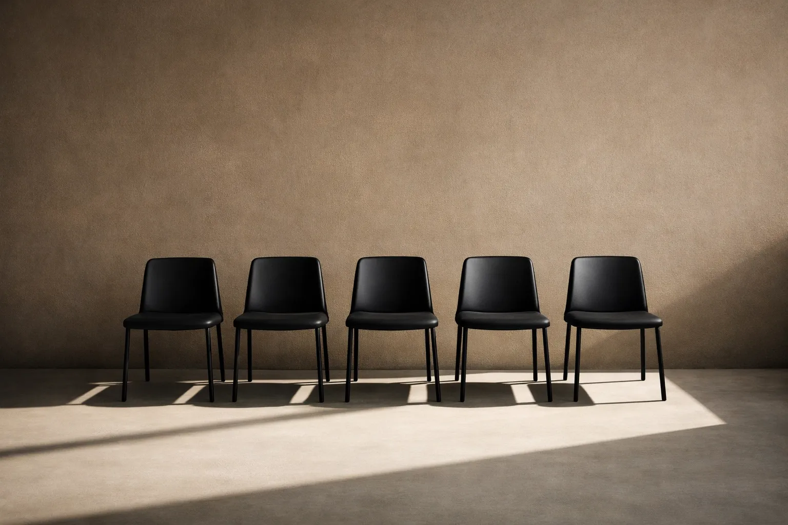 Minimalist black chairs against a wall representing the professional scrutiny and pressure of external authority.